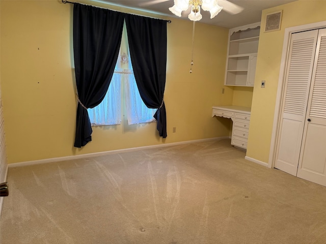 unfurnished bedroom with light carpet, a closet, ceiling fan, and built in desk