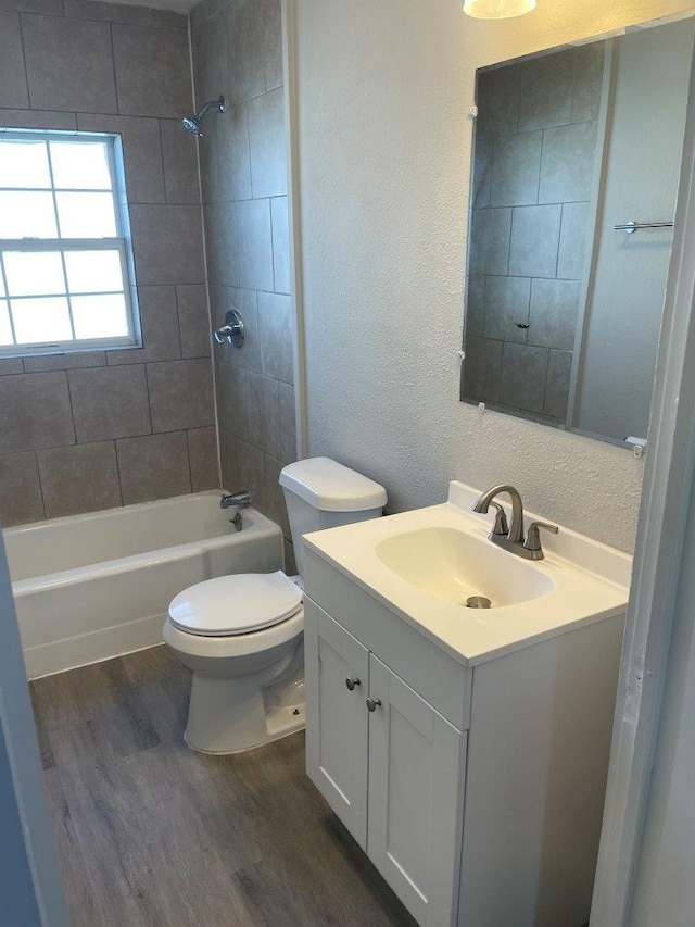 full bathroom featuring tiled shower / bath combo, toilet, hardwood / wood-style flooring, and vanity with extensive cabinet space