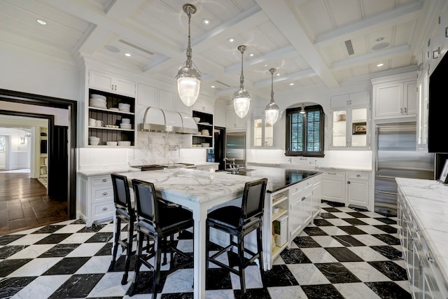 kitchen featuring an island with sink, a kitchen breakfast bar, backsplash, decorative light fixtures, and white cabinetry