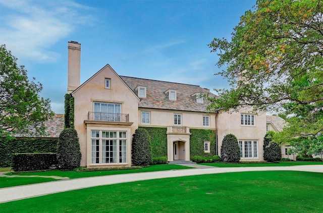 tudor home with a front lawn, a balcony, and french doors