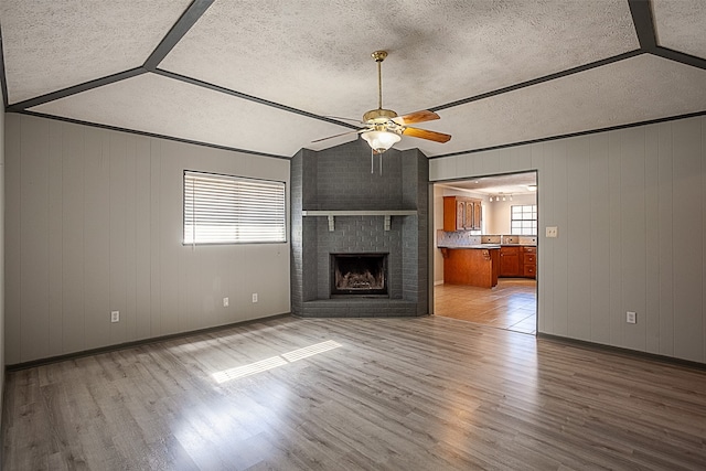 unfurnished living room featuring ceiling fan, light hardwood / wood-style floors, a brick fireplace, and vaulted ceiling