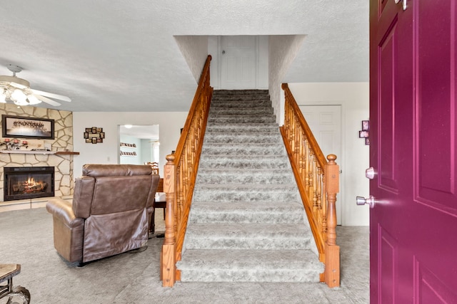 stairway with ceiling fan, a fireplace, carpet, and a textured ceiling