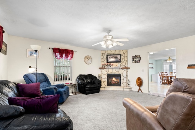 carpeted living room featuring plenty of natural light, ceiling fan, a stone fireplace, and a textured ceiling