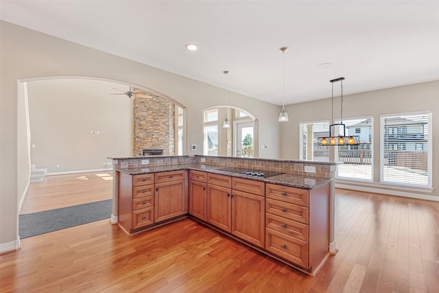 kitchen with dark stone countertops, hanging light fixtures, ceiling fan with notable chandelier, and light wood-type flooring