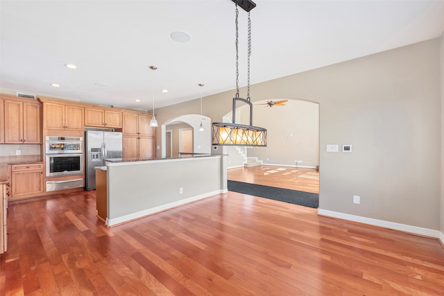 kitchen featuring decorative light fixtures, stainless steel appliances, dark stone counters, and hardwood / wood-style flooring