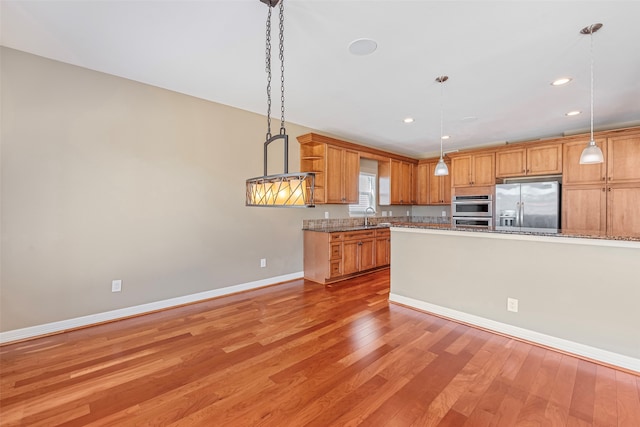 kitchen with stone counters, pendant lighting, sink, stainless steel appliances, and light hardwood / wood-style flooring