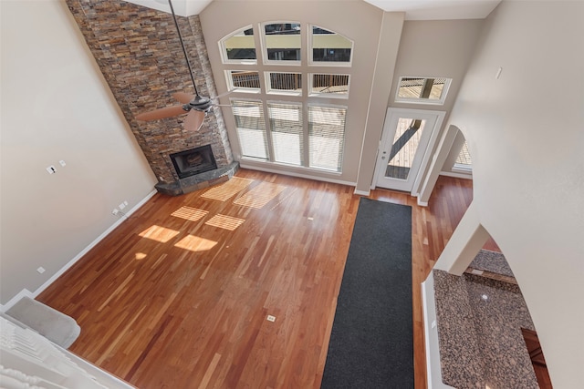 unfurnished living room with hardwood / wood-style flooring, ceiling fan, a stone fireplace, and a high ceiling