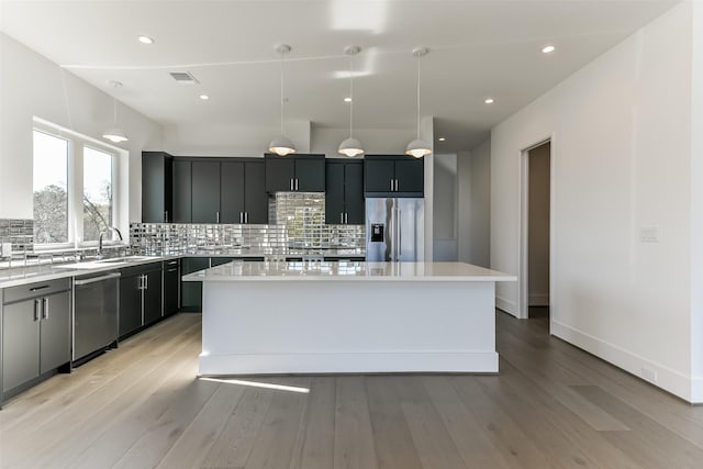 kitchen with backsplash, stainless steel appliances, decorative light fixtures, light hardwood / wood-style floors, and a kitchen island