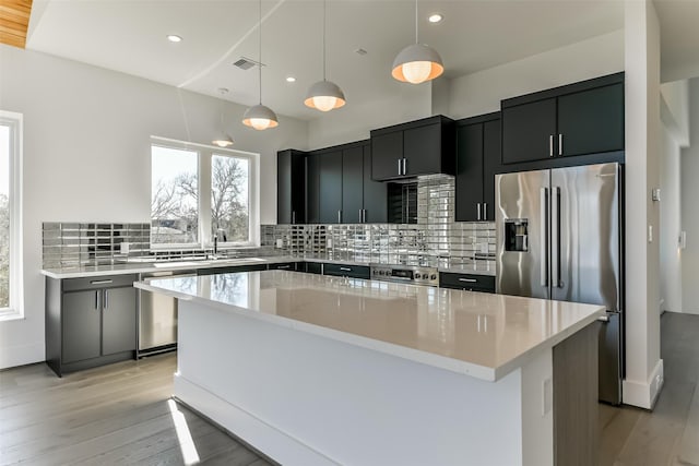 kitchen featuring stainless steel appliances, tasteful backsplash, light hardwood / wood-style floors, decorative light fixtures, and a kitchen island