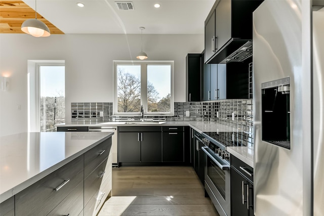 kitchen with backsplash, stainless steel appliances, sink, decorative light fixtures, and light hardwood / wood-style floors