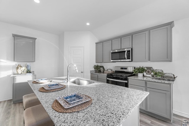 kitchen featuring gray cabinetry, a center island with sink, sink, appliances with stainless steel finishes, and light stone counters