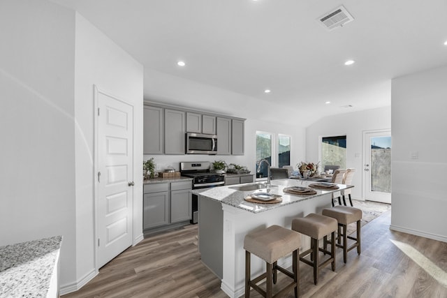 kitchen with light stone countertops, sink, gray cabinets, a kitchen island with sink, and appliances with stainless steel finishes