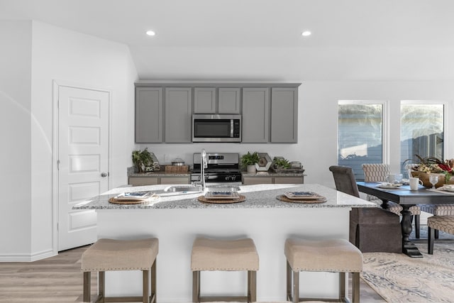 kitchen featuring a center island with sink, gray cabinets, light wood-type flooring, and stainless steel appliances