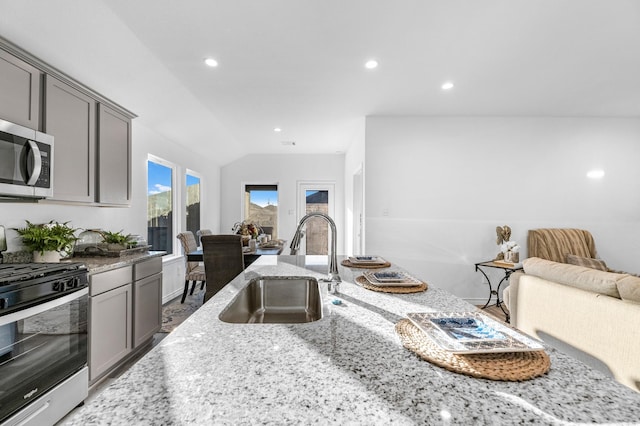 kitchen with lofted ceiling, sink, gray cabinets, appliances with stainless steel finishes, and light stone counters