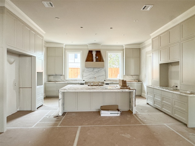 kitchen with decorative backsplash, sink, a center island, custom exhaust hood, and light stone counters