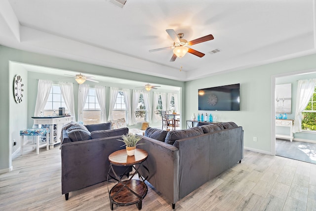 living room with light hardwood / wood-style flooring, a raised ceiling, and ceiling fan