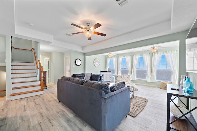 living room with a tray ceiling, light hardwood / wood-style floors, and ceiling fan