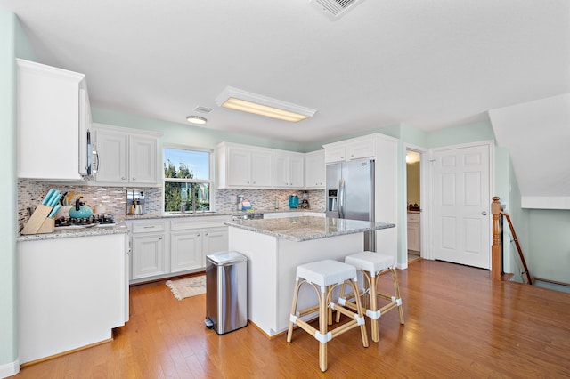 kitchen featuring light hardwood / wood-style flooring, stainless steel appliances, white cabinets, a center island, and light stone counters