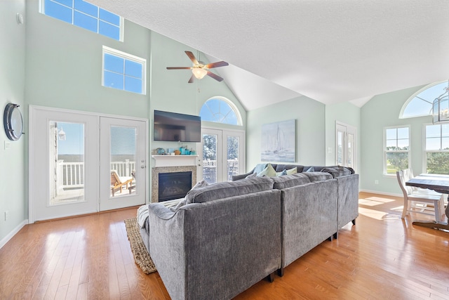 living room with ceiling fan, light hardwood / wood-style floors, a textured ceiling, high vaulted ceiling, and french doors