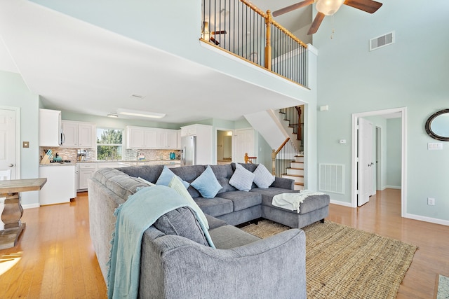 living room featuring ceiling fan, light wood-type flooring, and a towering ceiling