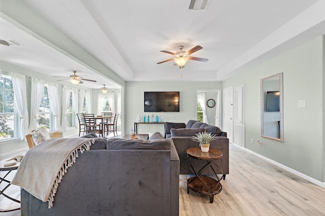 living room with ceiling fan, a tray ceiling, and light wood-type flooring