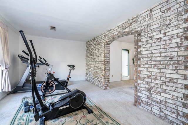 workout room featuring brick wall, ornamental molding, and light colored carpet