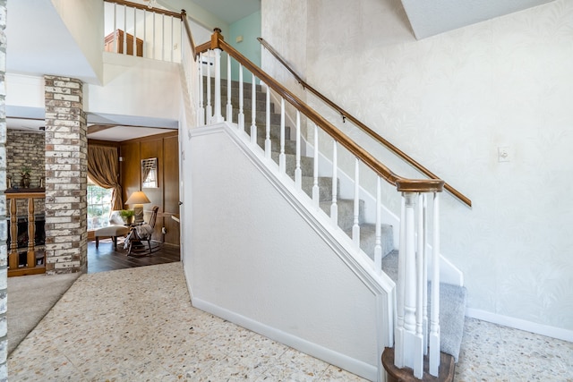 stairs featuring brick wall, light wood-type flooring, and ornate columns