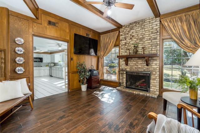 living room featuring ceiling fan, a fireplace, dark wood-type flooring, and beamed ceiling