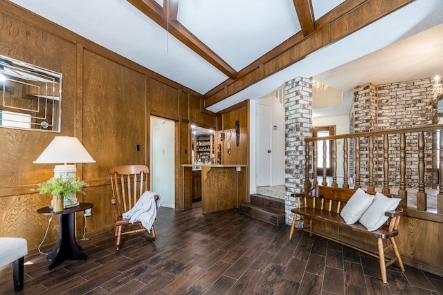 living area featuring vaulted ceiling with beams, dark wood-type flooring, brick wall, wood walls, and ornate columns