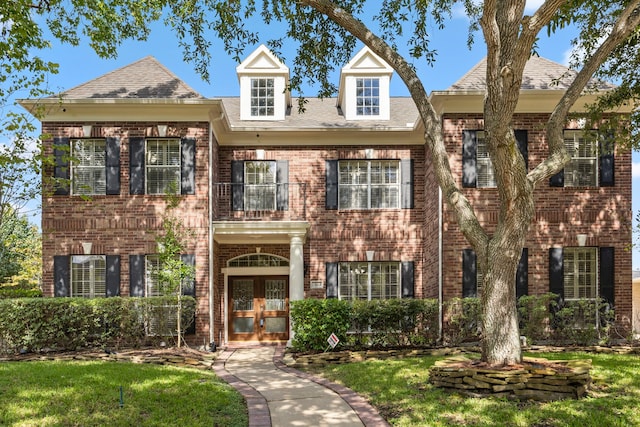 colonial-style house featuring a balcony, a front yard, and french doors