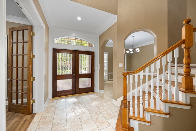 tiled foyer entrance featuring french doors, ornamental molding, a notable chandelier, and a towering ceiling