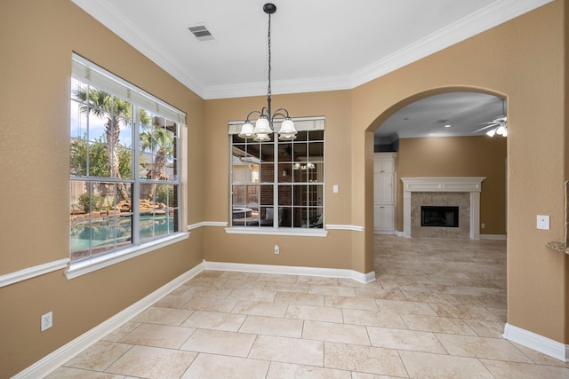 unfurnished dining area with a tiled fireplace, crown molding, ceiling fan with notable chandelier, and light tile flooring