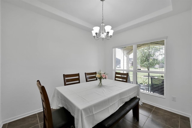 dining area with a chandelier, dark tile floors, and a raised ceiling