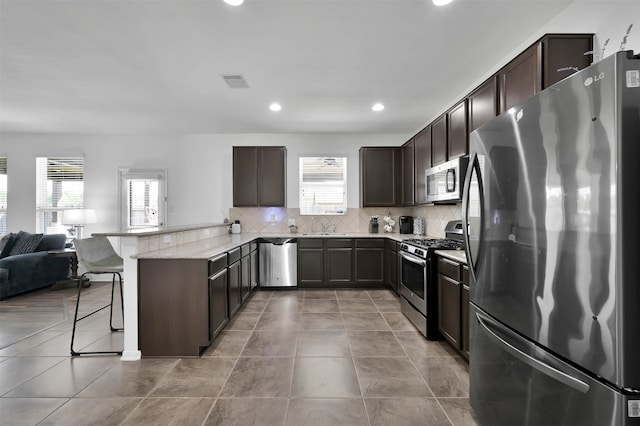 kitchen with light tile flooring, tasteful backsplash, a breakfast bar area, stainless steel appliances, and light stone countertops