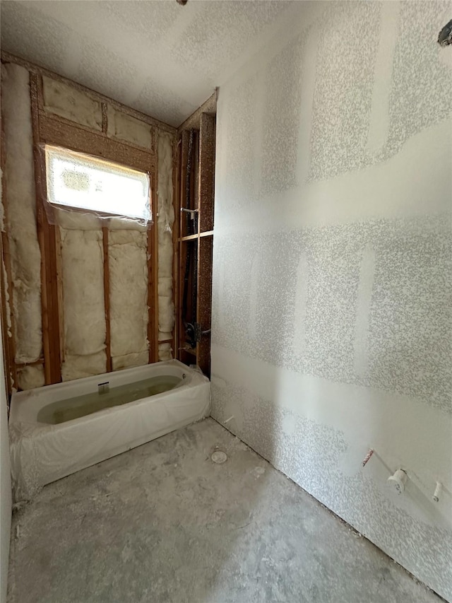 bathroom with a tub, concrete floors, and a textured ceiling