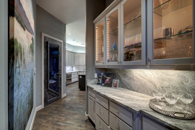 bar with tasteful backsplash, dark wood-type flooring, light stone counters, and gray cabinets