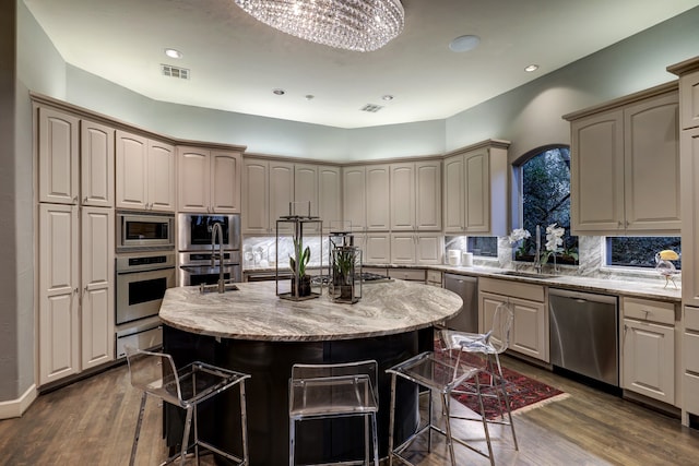 kitchen featuring dark hardwood / wood-style flooring, a breakfast bar, a center island with sink, stainless steel appliances, and an inviting chandelier