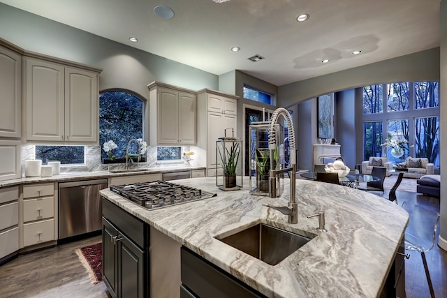 kitchen featuring dark wood-type flooring, light stone counters, tasteful backsplash, stainless steel appliances, and a kitchen island with sink