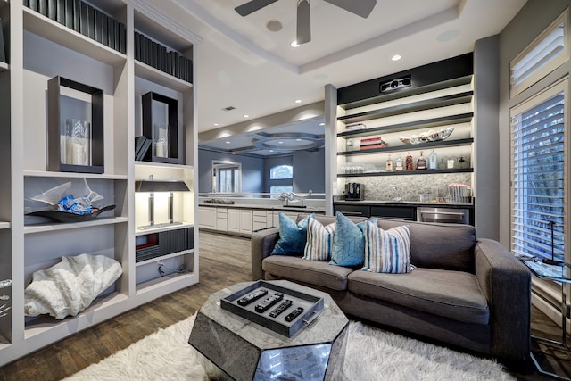 living room with a tray ceiling, ceiling fan, and dark wood-type flooring