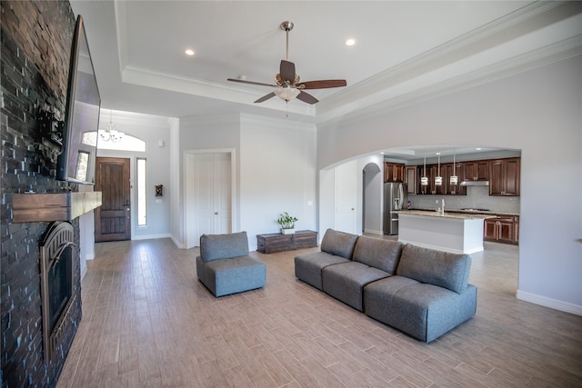 living room with a raised ceiling, light hardwood / wood-style flooring, ceiling fan with notable chandelier, and a fireplace