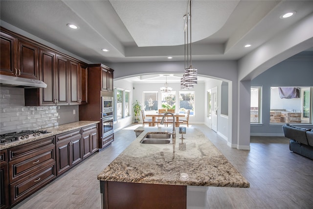 kitchen with sink, a notable chandelier, stainless steel gas cooktop, hanging light fixtures, and a raised ceiling