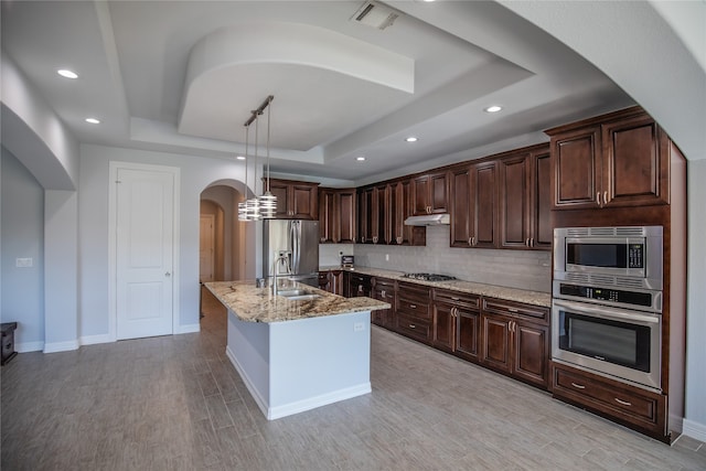 kitchen with light stone countertops, decorative light fixtures, appliances with stainless steel finishes, a raised ceiling, and tasteful backsplash