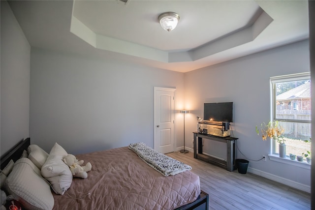 bedroom with light hardwood / wood-style flooring and a tray ceiling