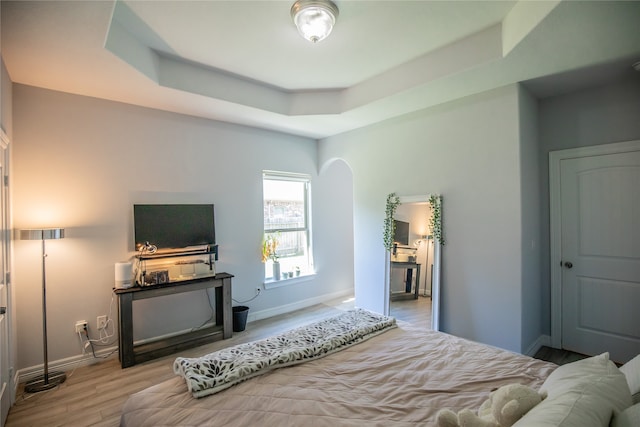 bedroom with light wood-type flooring and a raised ceiling