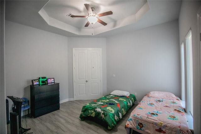 bedroom with ceiling fan, a closet, a raised ceiling, and light hardwood / wood-style floors