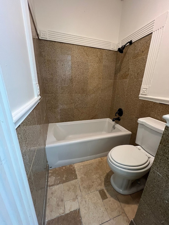 bathroom featuring tile walls, tiled shower / bath combo, toilet, and tile floors