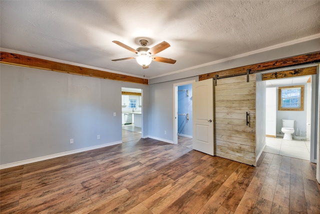 empty room with a barn door, ceiling fan, a textured ceiling, and dark hardwood / wood-style flooring