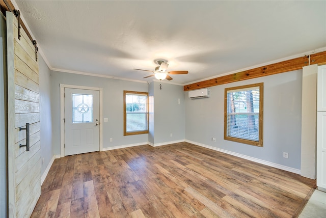 foyer featuring a barn door, ceiling fan, a wall mounted AC, ornamental molding, and light wood-type flooring