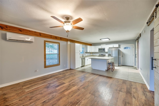 kitchen with a kitchen breakfast bar, an AC wall unit, ceiling fan, appliances with stainless steel finishes, and white cabinetry