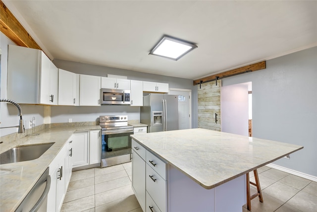 kitchen with sink, a kitchen island, appliances with stainless steel finishes, a barn door, and white cabinetry